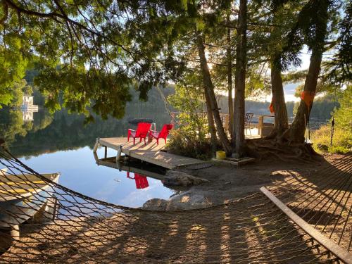two red chairs sitting on a dock next to a lake at Waterfront Chalet Serendipity Hideaway - Cachette Sérendipité - Swim SUPs BBQ Relax w Wifi in Chertsey