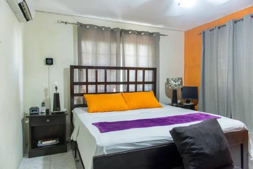 a bedroom with a large bed with an orange and white blanket at The Biltons - 6 min from airport- A/C in all rooms in Montego Bay