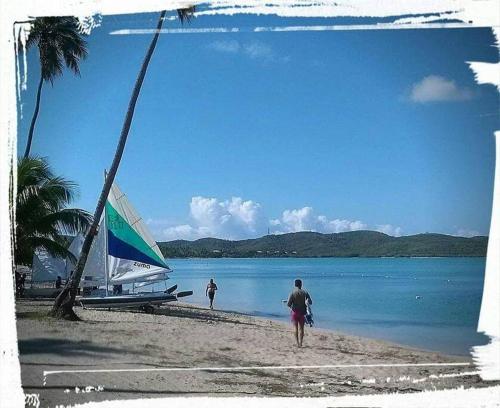 two people walking on a beach with a boat in the water at Beach House-Villa Taina, Boqueron Deposit Required in Cabo Rojo