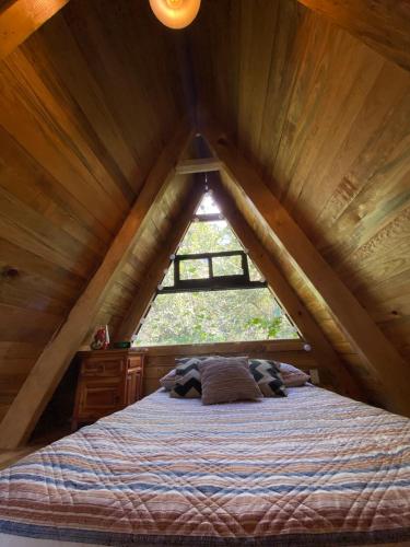 a bed in a attic with a large window at Cabañas Alpina, romántica y acogedora a 10 minutos del centro in Tepoztlán