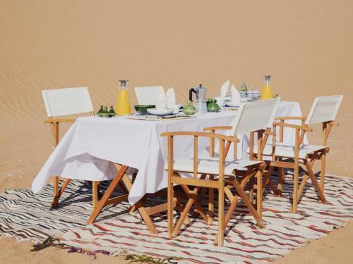 Mhamid Luxury Camp في Mhamid: طاولة طعام مع كراسي وطاولة بيضاء وكرسي