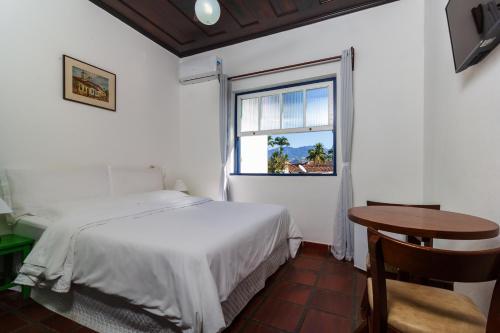 ein Schlafzimmer mit einem Bett und einem Tisch und einem Fenster in der Unterkunft Pousada Aconchego in Paraty