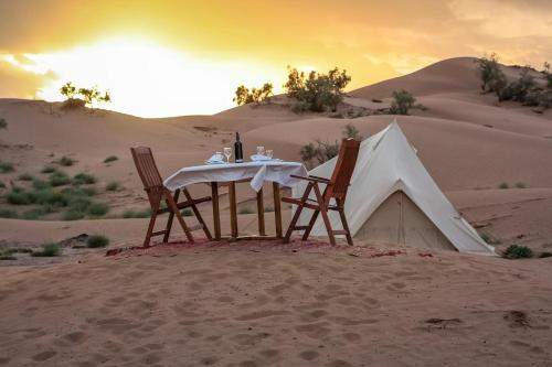 Mhamid Luxury Camp في Mhamid: طاولة و كرسيين و خيمة في الصحراء