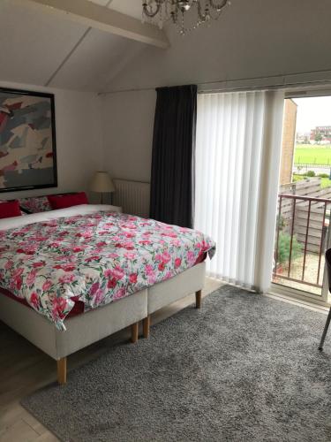 a bedroom with a bed with a floral bedspread and a window at Villa 't Haasduin in Wijk aan Zee