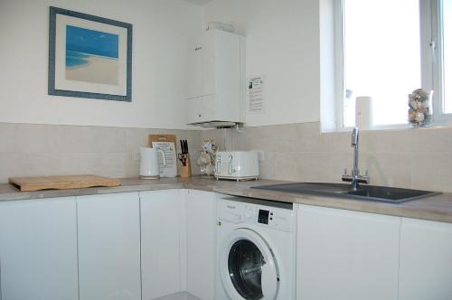 cocina blanca con lavadora y fregadero en Chwerthin Y Mor Beach House en Tywyn
