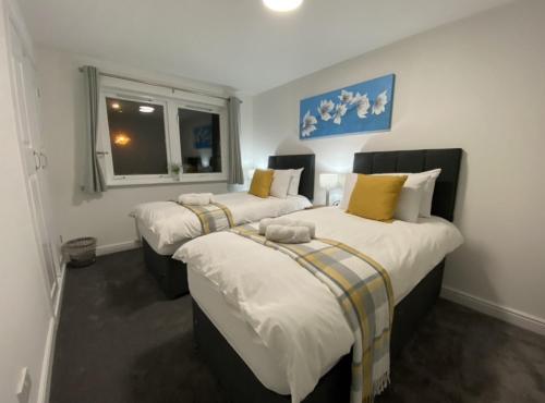 a bedroom with three beds with white and yellow pillows at Prime Dalgety Bay Waterfront Apartment in Saint Davids