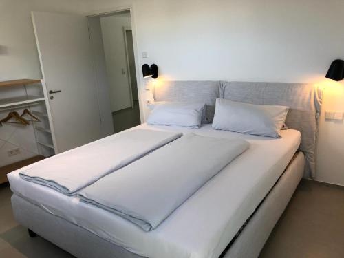 uma cama grande com lençóis brancos e almofadas em seenahe Design-Ferienwohnung Loft Aquamarin em Überlingen