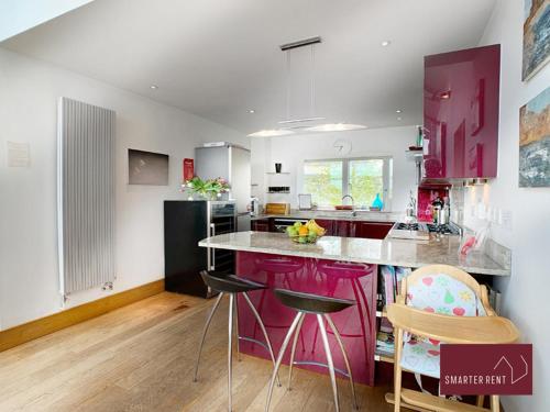 a kitchen with pink cabinets and a counter with stools at Clearwater - Lower Mill in Somerford Keynes