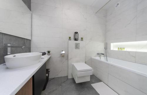 La salle de bains blanche est pourvue d'un lavabo, d'une baignoire et de toilettes. dans l'établissement Солнечные просторные апартаменты Метро Минская, à Kiev