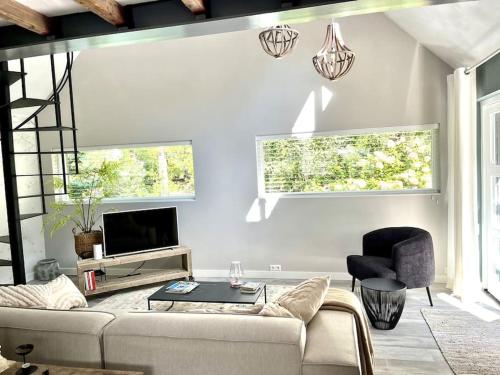 a living room with a couch and a tv and two windows at Vakantiehuis De koolmees, in een bosrijke natuur. in Kaatsheuvel