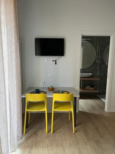 a dining table with two yellow chairs and a tv at Calari Rooms - Affittacamere in Bologna