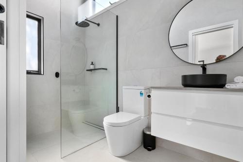 bagno bianco con servizi igienici e specchio di The Lake House & Apartment a Merimbula
