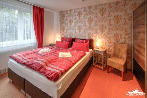 ein Schlafzimmer mit einem großen Bett mit roter Bettwäsche und einem Stuhl in der Unterkunft Auszeit-im-Harz Haus 6 in Wernigerode