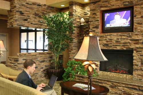 a man sitting on a couch with a laptop in front of a fireplace at Hampton Inn & Suites Farmington in Farmington