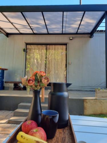 two black vases sitting on a table with fruit and flowers at Casa Container Camisão 