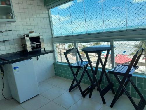 Duas cadeiras e uma mesa numa cozinha com uma janela em Belíssimo apartamento frente mar em Mongaguá