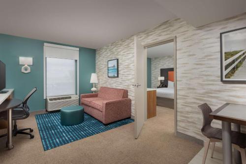a living room with a chair and a room with a bed at Home2 Suites by Hilton Jacksonville, NC in Jacksonville