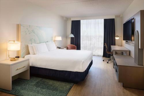 ein Hotelzimmer mit einem großen Bett und einem Schreibtisch in der Unterkunft Hotel Dello Ft Lauderdale Airport, Tapestry Collection by Hilton in Dania Beach