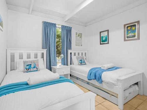 two beds in a white bedroom with blue curtains at Quarterdeck in Portsea