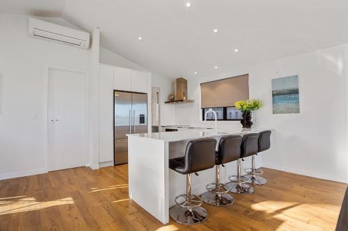 a white kitchen with a counter and stools at Waterfront Oasis - Omokoroa Holiday Home in Omokoroa