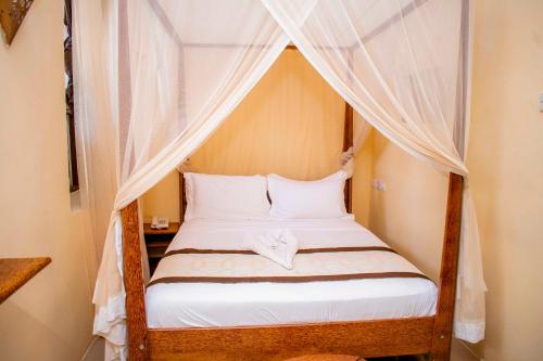 1 dormitorio con cama con dosel y sábanas blancas en The Island Stone Town hotel en Ngambo