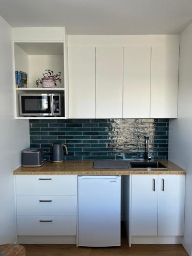 a kitchen with white cabinets and a sink and a microwave at Ohana in Whitianga