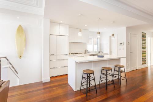 a kitchen with white cabinets and two bar stools at Cottesloe Aqua Retreat - Executive Escapes in Perth
