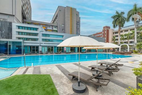 a pool with benches and umbrellas in front of a building at Guide Hotel Kaohsiung Liuhe in Kaohsiung