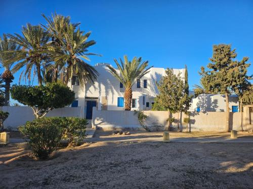 een wit huis met palmbomen en een hek bij App 2 chambres piscine privative 600m plage in Mezraya