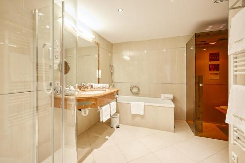 a bathroom with a tub and a sink and a shower at Hotel EDELWEISS Berchtesgaden Superior in Berchtesgaden
