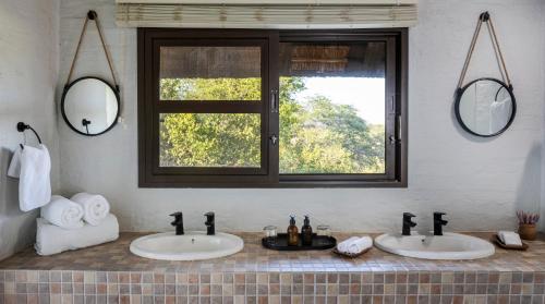 2 lavabos en un baño con 2 espejos en Simbavati Mvubu Cottage, en Reserva Timbavati