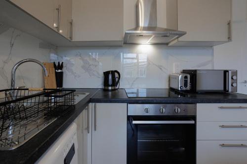 uma cozinha com armários brancos e um forno de fogão preto em Lovely 2-bed Highbury Home em Londres