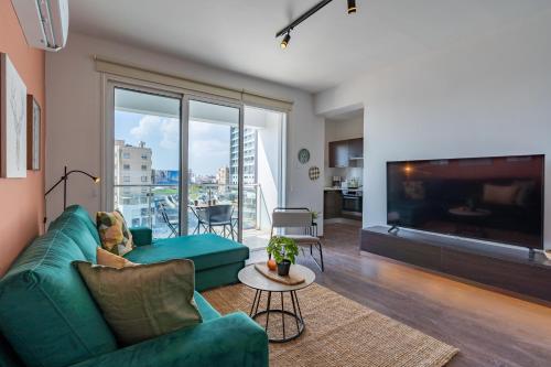 a living room with a green couch and a large window at Harbor Apartments in Larnaca in Larnaka