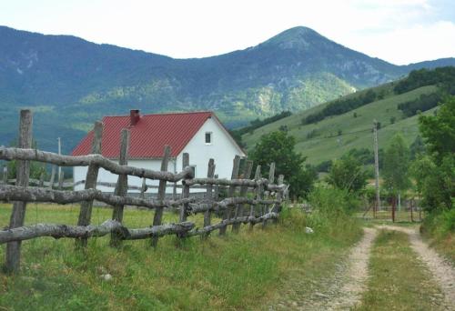 une clôture en face d'une maison blanche avec des montagnes dans l'établissement Matija, à Nikšić