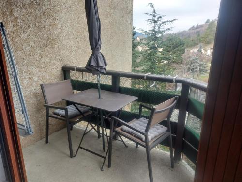un tavolo con due sedie e un ombrellone su un balcone di Appartement en résidence proche du plan d'eau a Embrun