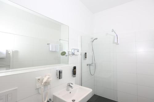 ein weißes Bad mit einem Waschbecken und einer Dusche in der Unterkunft H24 Hoteltow in Teltow