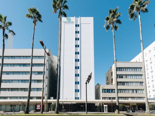 a tall white building with palm trees in front of it at Prince Smart Inn Miyazaki in Miyazaki