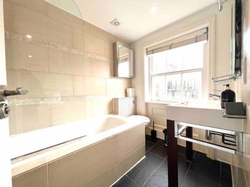 a bathroom with a tub and a sink and a window at Hyde Park- 1 Bed in London