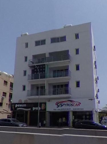 a tall white building with cars parked in front of it at Harbor Apartments in Larnaca in Larnaka