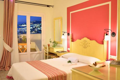 a hotel room with a bed and a desk and a window at Pelican Hotel in Mikonos