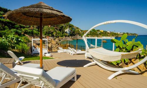 a deck with chairs and an umbrella and the ocean at Calanica Resort in Cefalù