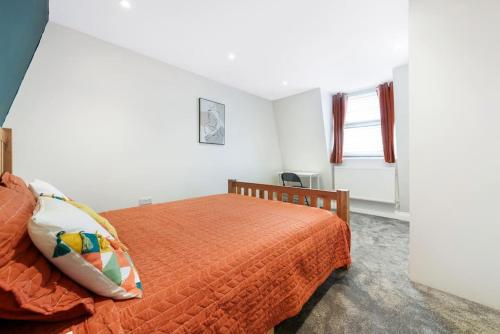 a bedroom with a bed with an orange comforter and a window at Stunning Double Rooms within a Loft space in London