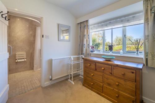 a bathroom with a wooden dresser and a window at Three Tuns Cottage in Little Walsingham