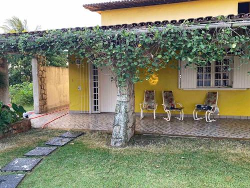 uma casa amarela com duas cadeiras e uma árvore em CASA EM GUARAPARI em Guarapari