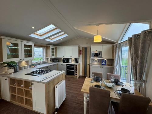 a kitchen with white cabinets and a table with a dining room at Golden Anchor - The Vogue - Coastal Caravan Breaks in Chapel Saint Leonards
