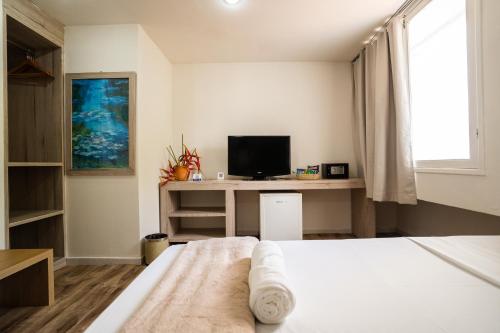 a bedroom with a bed and a desk with a television at Hotel Pipa Atlântico in Pipa