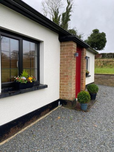 ein weißes Haus mit einer roten Tür und einigen Pflanzen in der Unterkunft Joe’s Cottage in Tynan