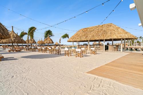 a beach with tables and chairs and straw umbrellas at The Rif At Mangrove Beach Corendon Curacao All-Inclusive, Curio by Hilton in Willemstad