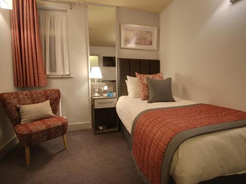 um quarto de hotel com uma cama e uma cadeira em The Suffolk Hotel em Haverhill