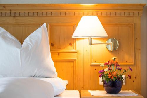 a bedroom with a bed with a lamp and a vase with flowers at Hotel Regina in Soprabolzano